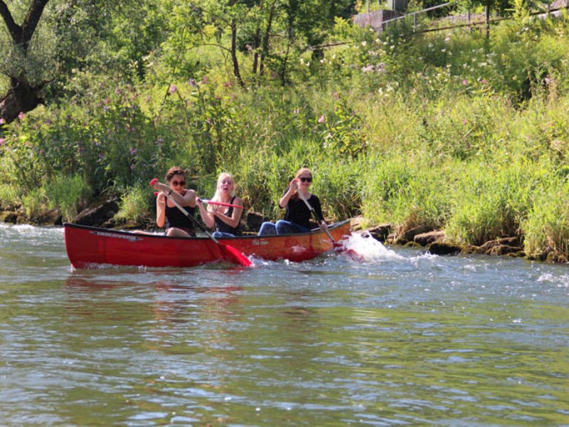 3 Frauen bei Paddeluebung in rotem Kanu, Steuern mit Paddel üben, quer zur Strömung