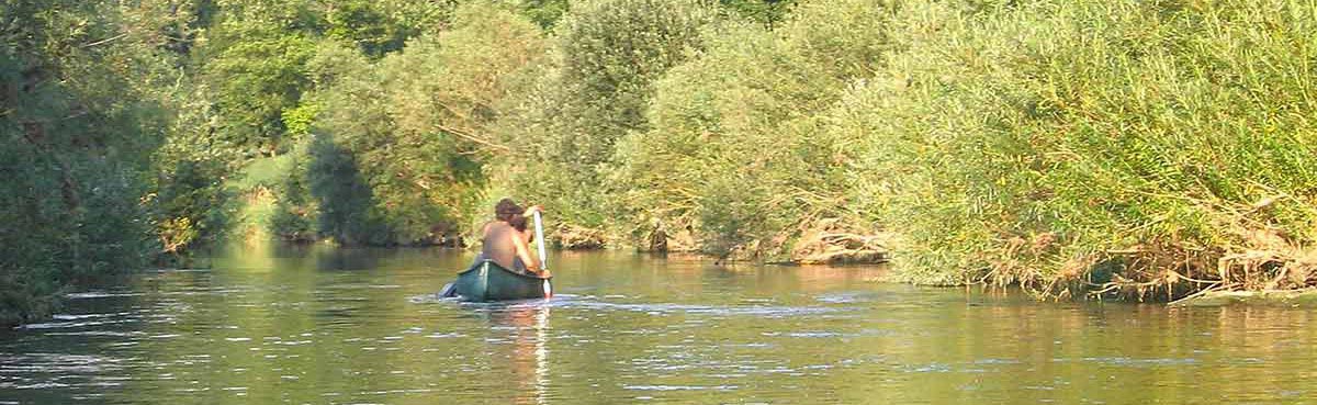 Paddeln Ein Kanu von hinten in der Mitte des Bilds mit 3 Personen. Links und rechts Büsche