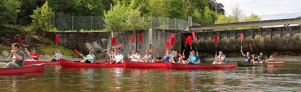 Gruppenfahrt Gruppenfahrt. Mehrere rote Kanus auf Fluss vor Ufer und Mauer, strecken Paddel hoch