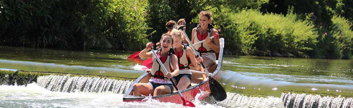 Staustufe Ein rotes Kanu mit 3 paddelnden jungen Frauen fährt durch Staustufe. Foto von schräg vorne am rechten Bildrand; dahinter zweites Boot, verdeckt durch erstes Boot.